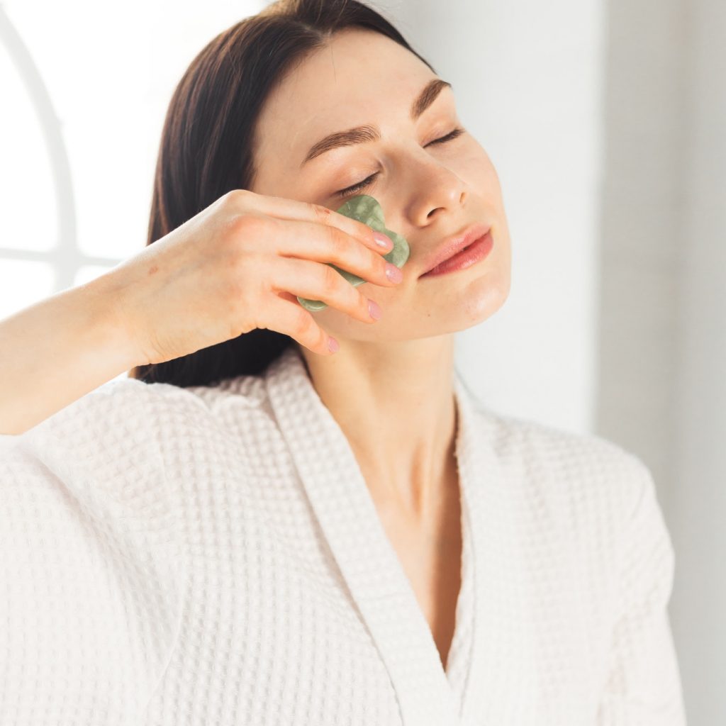 Young woman doing face Gua sha - chinese traditional massage
